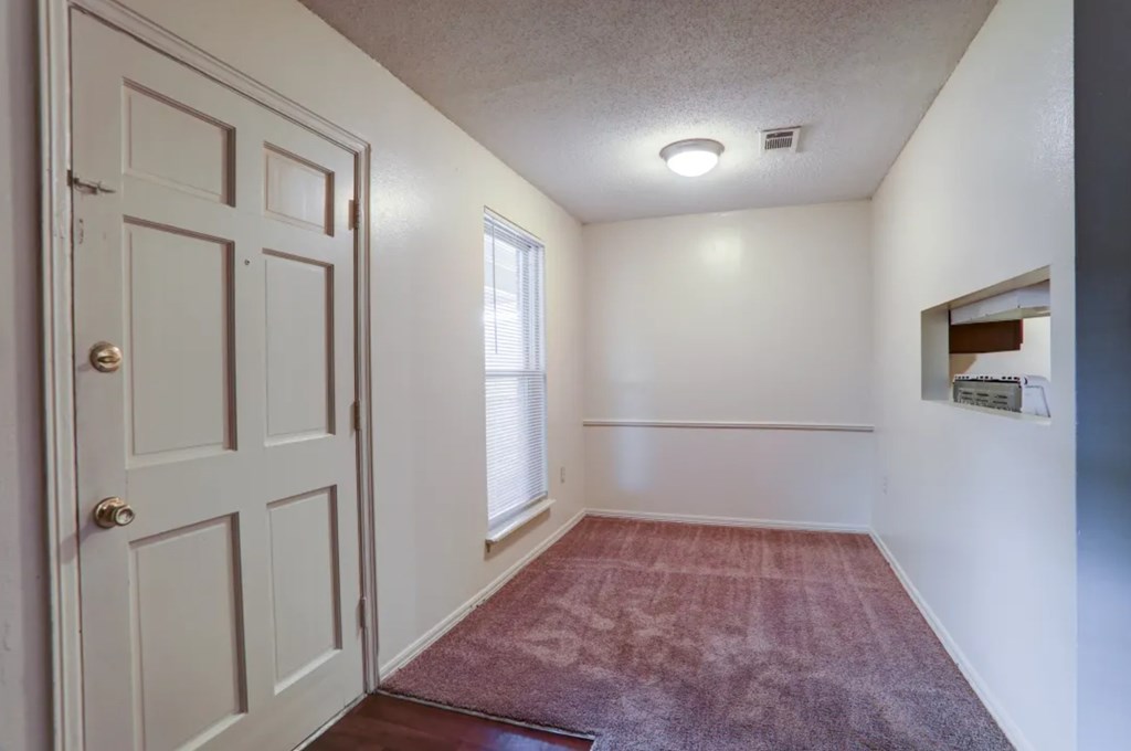 A room with a white door, a window, and a red carpet.